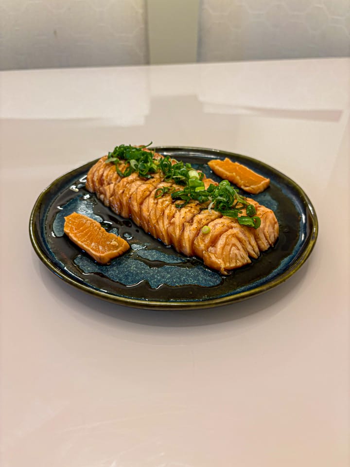 Salmão fatiado ao molho teriyaki com cebolinha, em prato de cerâmica azul-petróleo